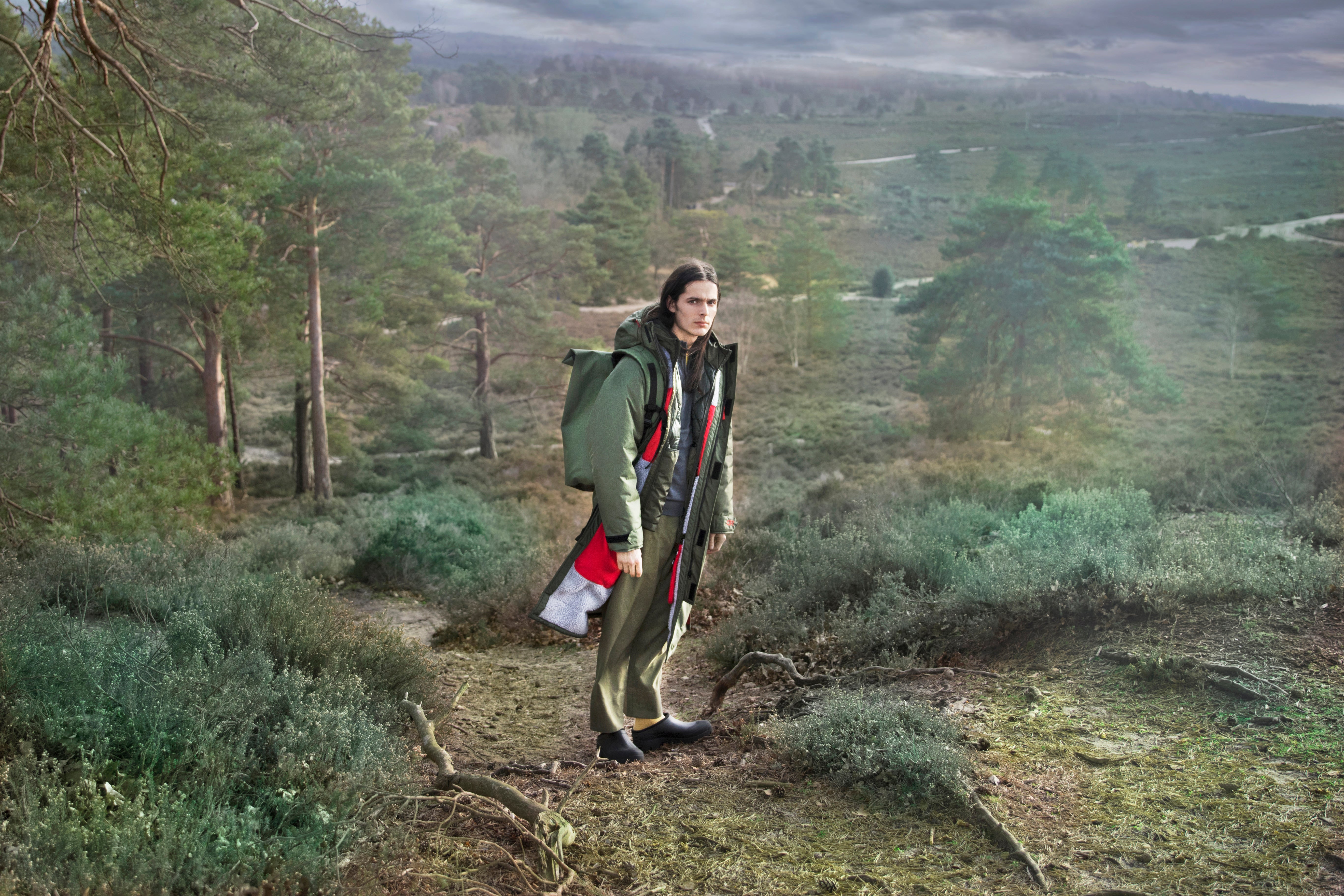 A man tracking a beautiful lush green forest wearing an oversized green dry robe and carrying a green backpack to match his robe. These hooded unisex changing robes by D-Robe are made from recycled materials, with a waterproof outer, fleece-lined inner, waterproof pockets, adjustable hood and cuffs.