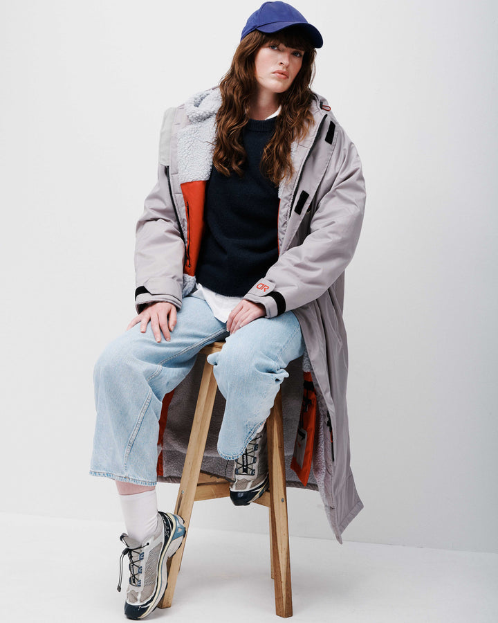 A woman laying on a field wearing a stylish, oversized drying robe. These hooded changing robes for men and women are made from recycled material and are, waterproof, wind-resistant and breathable. They are perfect for all year round.